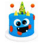 Colorful Blue Monster Party Cake with textured blue fur design, large eyes, a wide smiling mouth, orange cheeks, two yellow horns, and a green party hat with a gold number 2 on top