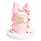 Pink Bow Ruffle Cake with a tall cylindrical shape covered in light pink frosting, decorated with a large satin pink bow and ruffled fondant accents, featuring gold "Happy Birthday" lettering.