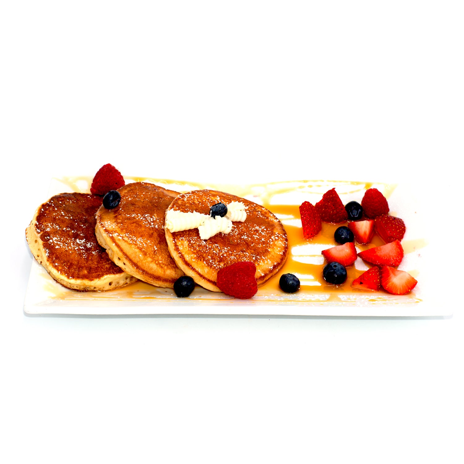 Fluffy pancakes with butter and syrup, served with fresh strawberries, blueberries, and raspberries on a white rectangular plate.