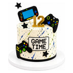 Game Time Cake featuring a white base with colorful splatter design, decorated with edible gaming controllers, black stars, and a gold number 12 topper.