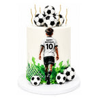 All Sports Champion Cake featuring a soccer-themed design with a boy in a jersey walking towards a pile of soccer balls on top, decorated with green grass and goal net details.
