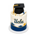 UCLA Graduation Cake featuring a black graduation cap with gold tassel and a rolled diploma on a white and blue base, decorated with gold accents, luxury custom cakes baked fresh in Beverly Hills.