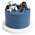 Blue cake decorated with gold speckles and small gold balls topped with edible game controller and smartphone shapes, along with black, silver, and dark blue spherical decorations.