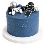 Blue cake decorated with gold speckles and small gold balls topped with edible game controller and smartphone shapes, along with black, silver, and dark blue spherical decorations.