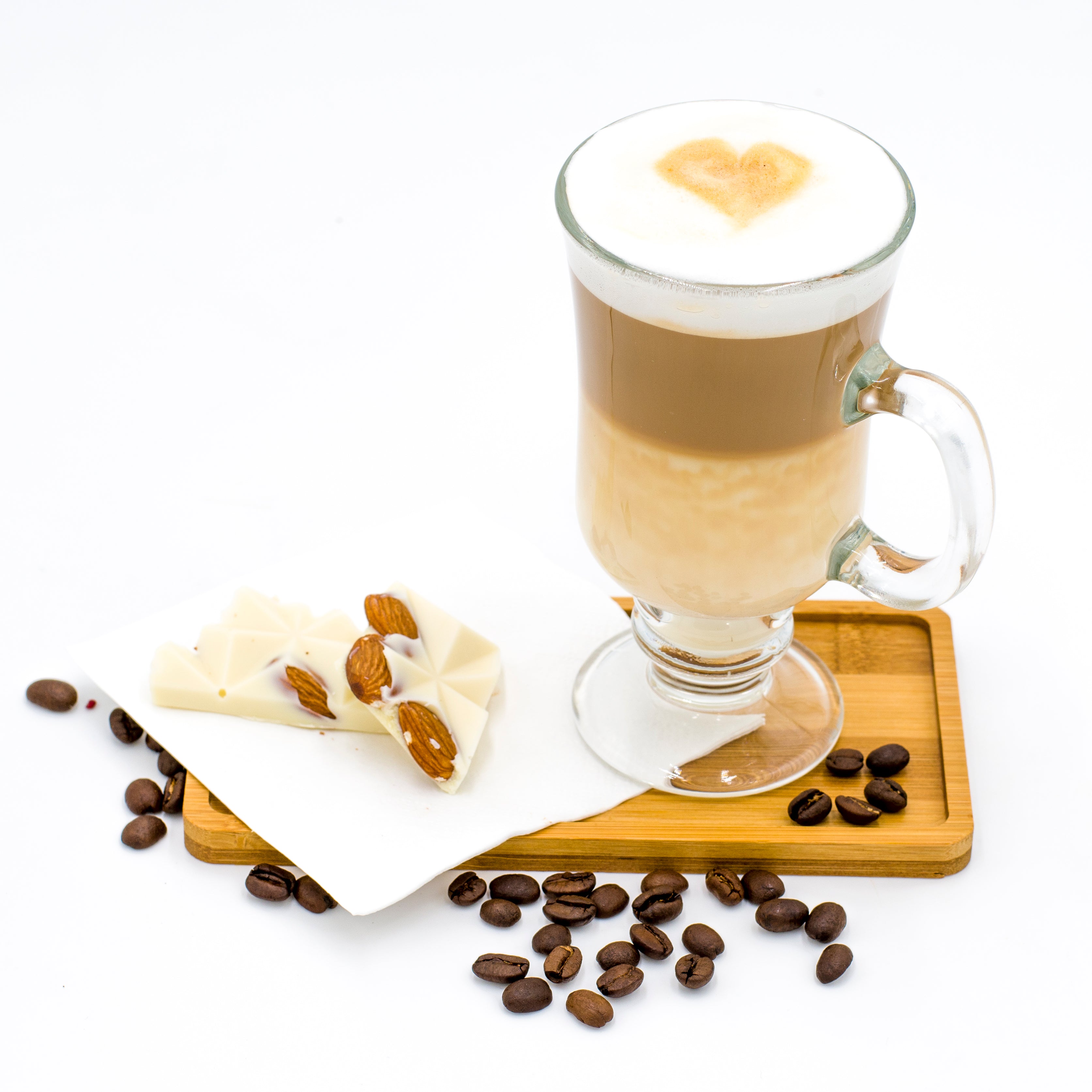 Latte with heart latte art in glass mug, white chocolate almond bark, coffee beans on tray