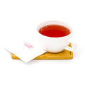 Cup of red herbal tea in white mug on wooden tray with branded napkin
