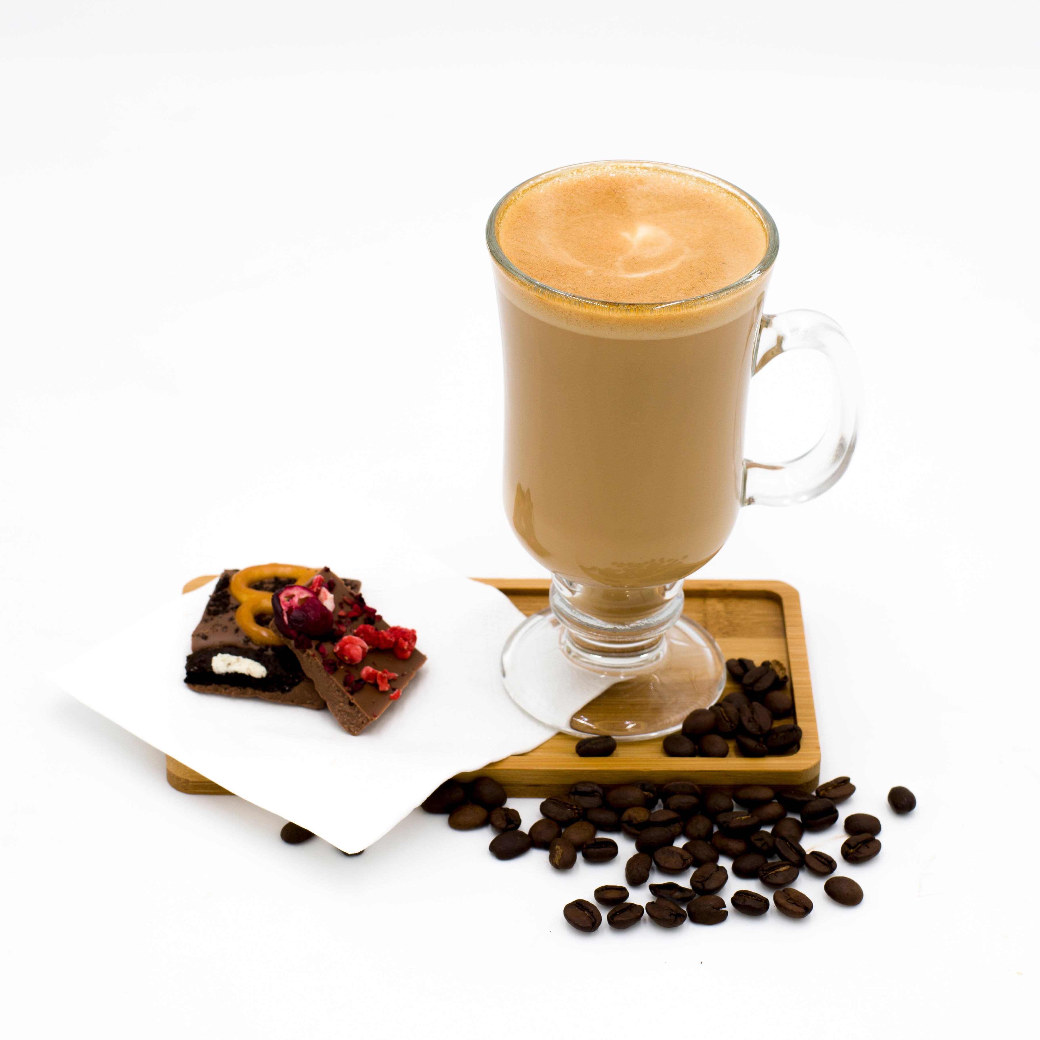 Glass of cappuccino with gourmet chocolate pieces on a wooden tray and coffee beans on white