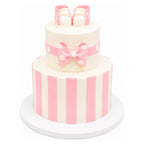 Two-tier custom cake decorated with vertical pink and white stripes, a pink bow with white polka dots, and topped with pink stripe baby booties cake accents.