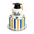 Two-tier UCLA Graduation Cake – Striped Edition with blue and gold stripes, quilted top tier, cake topper in the shape of graduation cap, custom cakes by luxury bakery on Rodeo Drive.